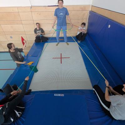 6 Frauen sind am und auf dem Trampolin und machen mit einem Reifen und Seilen eine spielerische Übung