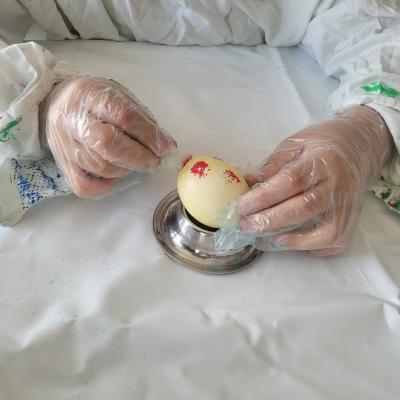 Eine Person tupft mit einem Schwämmchen rote Farbe auf ein gelbes Ei 