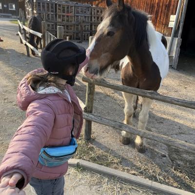 Ein Mädchen legt eine Kugel in eine Kugelbahn. Die Kugelbahn ist draußen an einer Mauer angebracht.