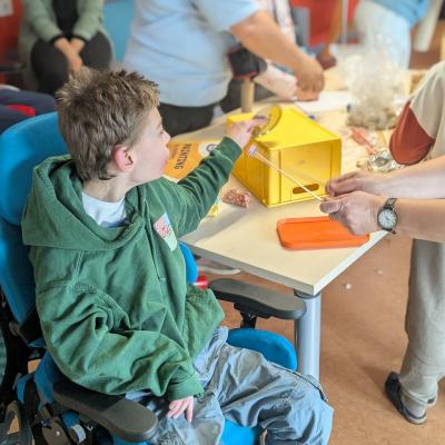 Ein Junge sitzt im Therapeistuhl und steht am Basteltisch