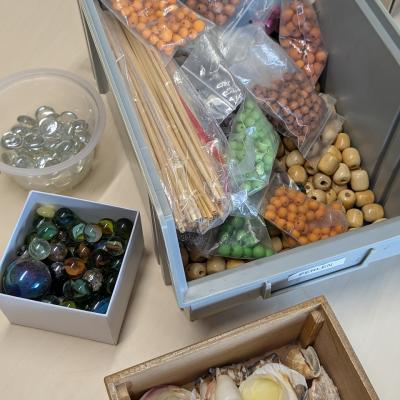 Bastelmaterialien stehen auf dem Tisch. Perlen, Murmeln, Steine, Muscheln