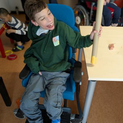 Ein Junge im Therapeistuhl schüttelt eine selbstgebaute Rassel und freut sich sehr 