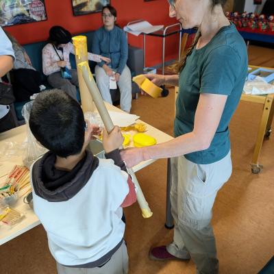 Ein Junge und eine Frau basteln zusammen mit einer langen Röhre