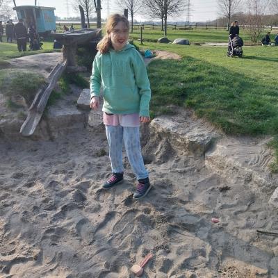 chülerin steht im Sandkasten, schaut in die Kamera und freut sich dass das Wetter schön ist 