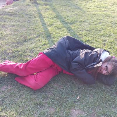 Schülerin mit schwarzer Jacke, roter Hose, liegt auf dem Rasen und lacht 