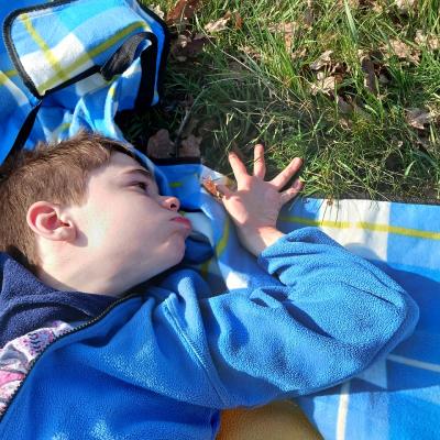 Schüler liegt mit blauer Jacke auf einer Picknickdecke und fühlt das Gras
