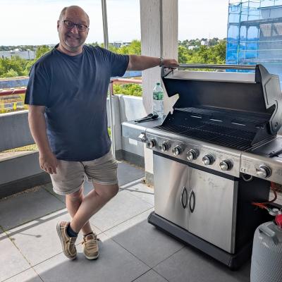 ein Mann steht am Grill und lacht in die Kamera