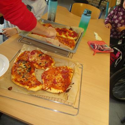 Ein Junge betrachtet im Klassenzimmer die frisch gebackenen Pizzastücke auf zwei Blechen