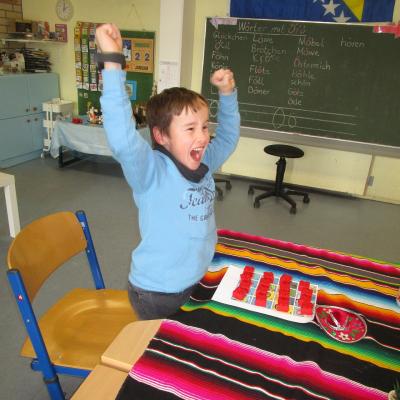 Ein Junge jubelt beim Lottospiel. Der Tisch im Klassenzimmer ist mit einer mexikanischen Decke geschmückt. 