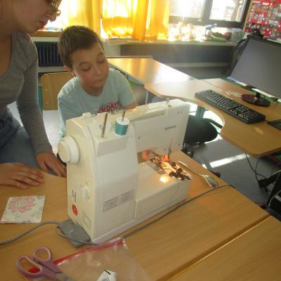 Ein Junge neben einer Erzieherin an der Nähmaschine im Klassenzimmer