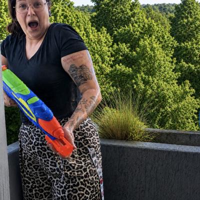 eine Frau wird bei einer Wasserschlacht nass gespritzt und schaut erschrocken in die Kamera