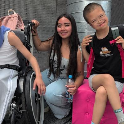 Muratcan, Fernanda und Henry sitzen vor einer grauen Wand und lächeln in die Kamera.