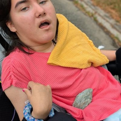 Ein Mädchen im Rollstuhl hat einen kleinen zauiberstein auf sich liegen 