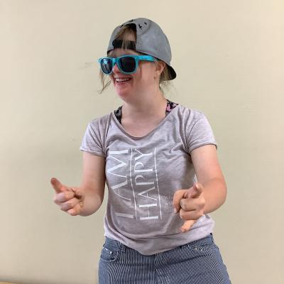 Eine junge Frau lacht, sie hat eine Mütze und eine Sonnenbrille auf 
