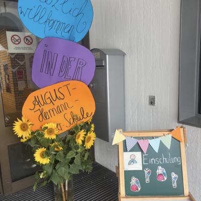 Begrüßung der neuen Erstklässler*innen durch gebastelte Schilder und Blumen vor dem Schuleingang. 