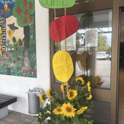 Begrüßung der neuen Erstklässler*innen durch gebastelte Schilder und Blumen vor dem Schuleingang. 