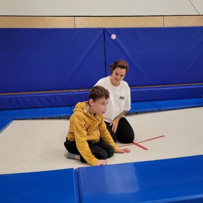 Ein Junge, der in der Sporthalle neben einer Frau auf dem Trampolin sitzt. 